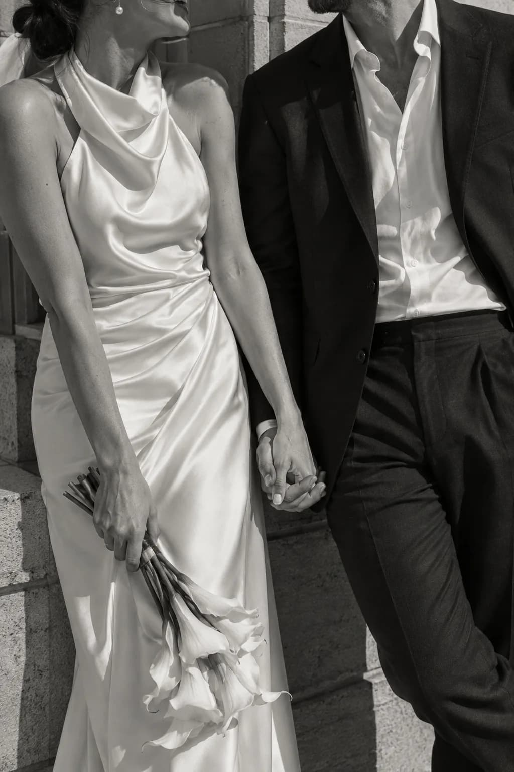 Two people dressed for their wedding, holding hands in bright afternoon light